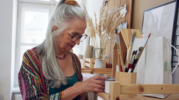 A creative senior woman artist taking colors and brushes in her artist studio.