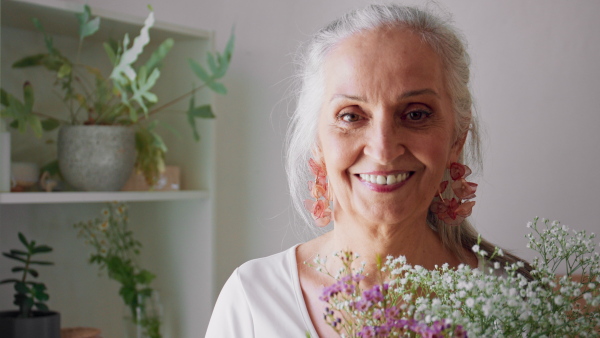 A happy senior woman with flowers looking at camera and smiling at home.