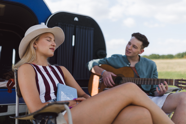 Happy young couple sitting together in front of van, camping and playing at a guitair.