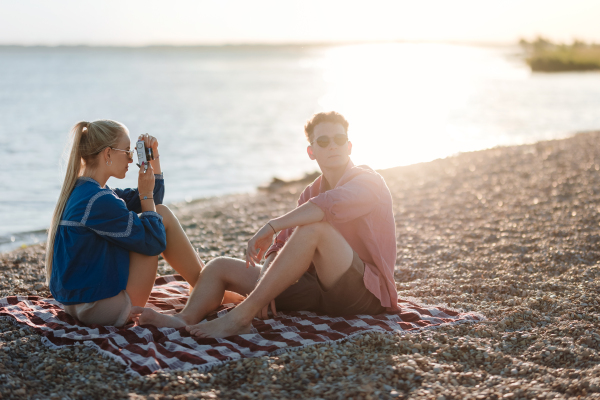 Young girl taking a photo of her boyfriend at beach during sunset.