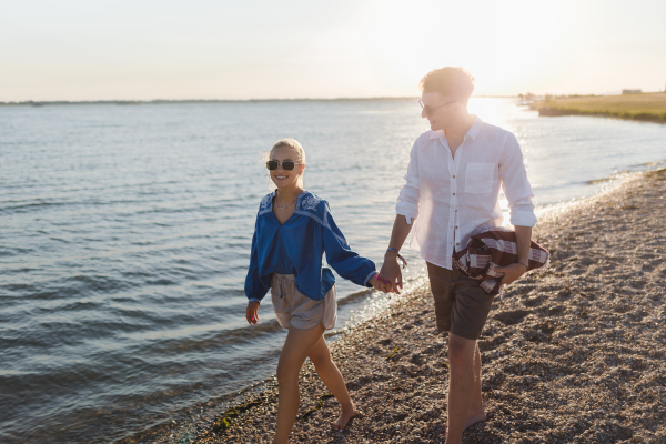 Happy young couple with blanket walking in the beach during sunset, prepairing for a picnic.