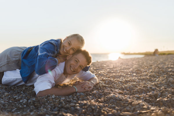 A happy young woman lying on her boyfriends back, looking at camera, having fun together.