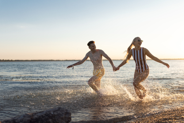 Happy young couple in the swimsuits runing in the sea, holding each other hand. Enjoying vacation time together.