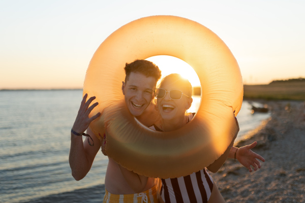 Happy young couple in swimsuits posing with orange swimming wheel, smiling and looking at camera.