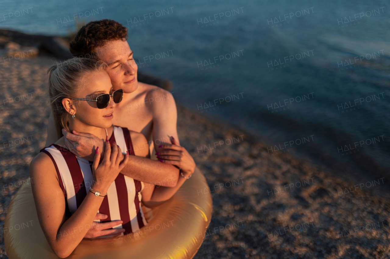 A happy young couple in swimsuits posing with swimming wheel, at beach during sunset.