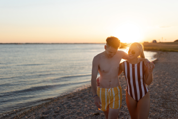 Happy young couple in the stripped swimsuits walking in the beach during sunset.