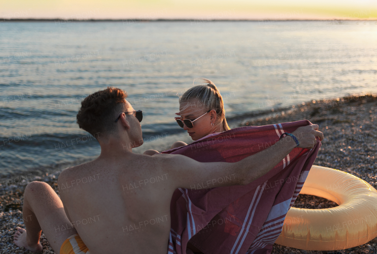 Young boy in a swimsuit getting blanket to his girlfriend in the beach, rear view.