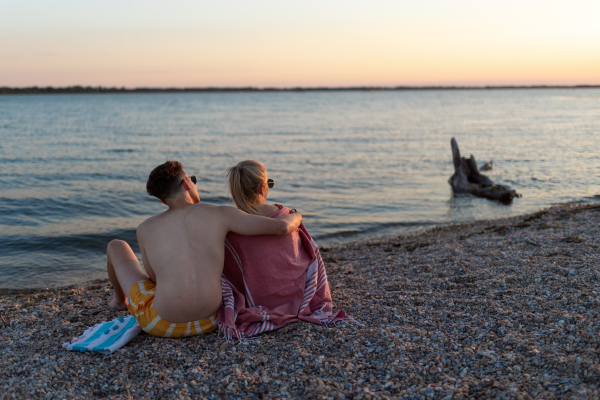 Young boy in a swimsuit getting blanket to his girlfriend in the beach, rear view.