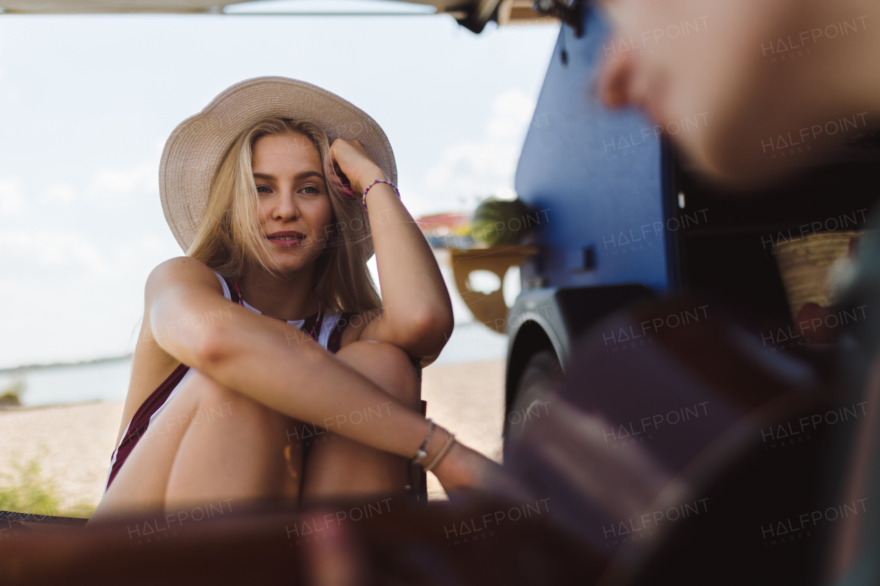 Happy young couple sitting together in front of van, camping and playing at a guitair.