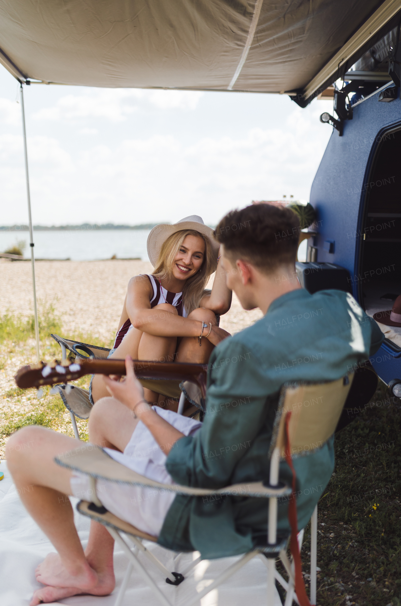 Happy young couple sitting together in front of van, camping and playing at a guitair.