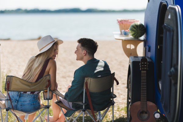 A young couple sitting together in front of van during summer vacation and talking.