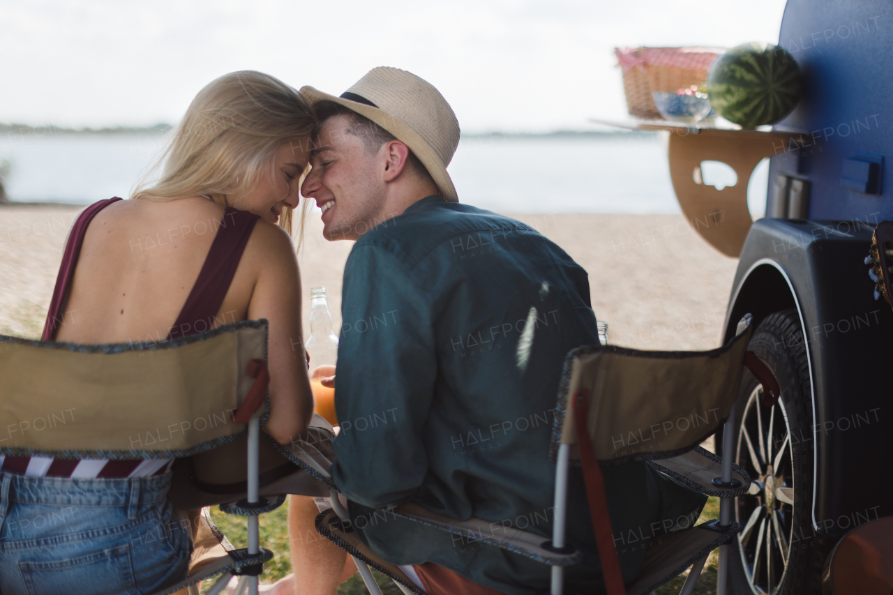 A young couple sitting together in front of van during summer vacation, bonding.