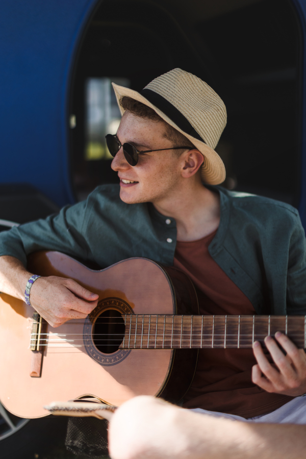 Young man sitting in van playing on the guitar,enjoying summer time.