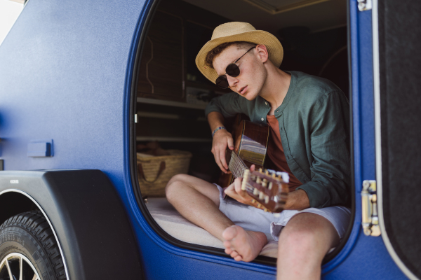 Young man sitting in van playing on the guitar,enjoying summer time.