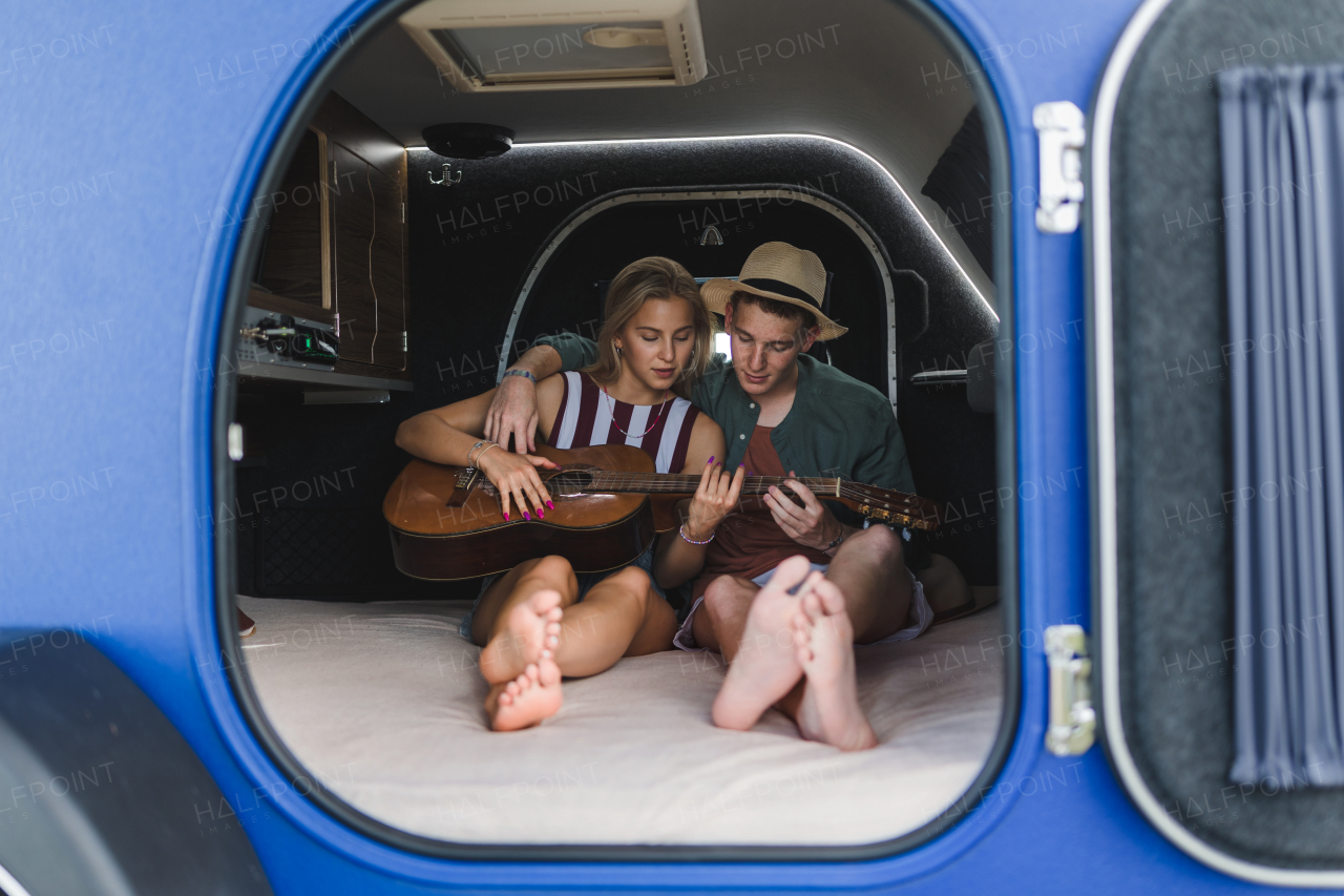 Happy young couple sitting together in a van, camping and playing at a guitair.