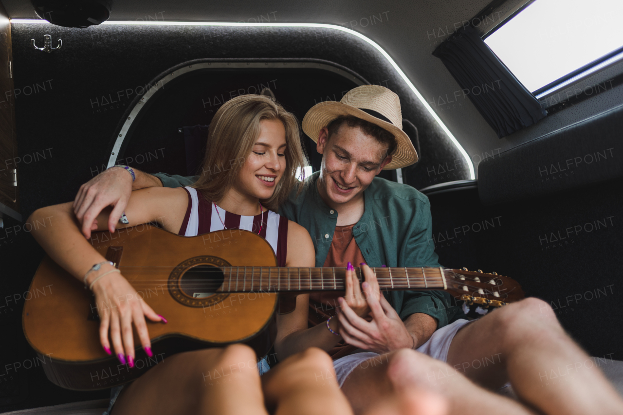 Happy young couple sitting together in a van, camping and playing at a guitair.