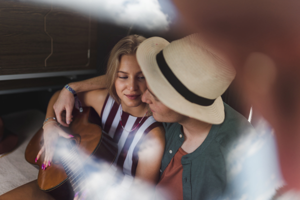 Happy young couple sitting together in a van, camping and playing at a guitair.