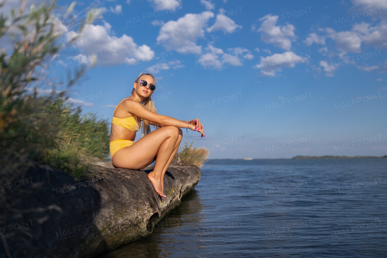 Young woman in a swimsuit sitting at lake, summer vacation concept.