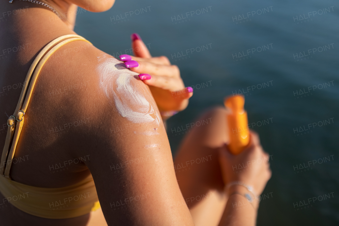 Close-up of young woman in yellow swimsuit applying suncreen on her skin, vacation and skin protection concept.