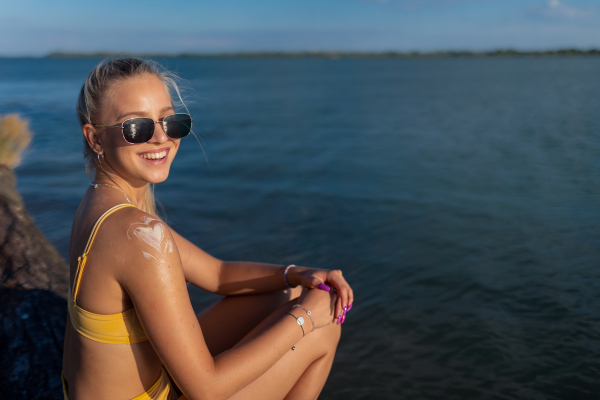 Close-up of young woman in yellow swimsuit applying suncreen on her skin, vacation and skin protection concept.