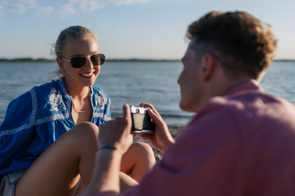 Young boy taking a photo of his beautiful girlfriend at beach during sunset.