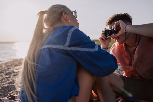 Young boy taking a photo of his beautiful girlfriend at beach during sunset.