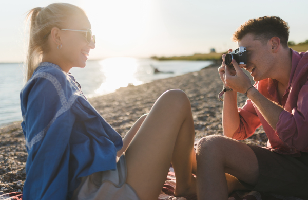 Young boy taking a photo of his beautiful girlfriend at beach during sunset.