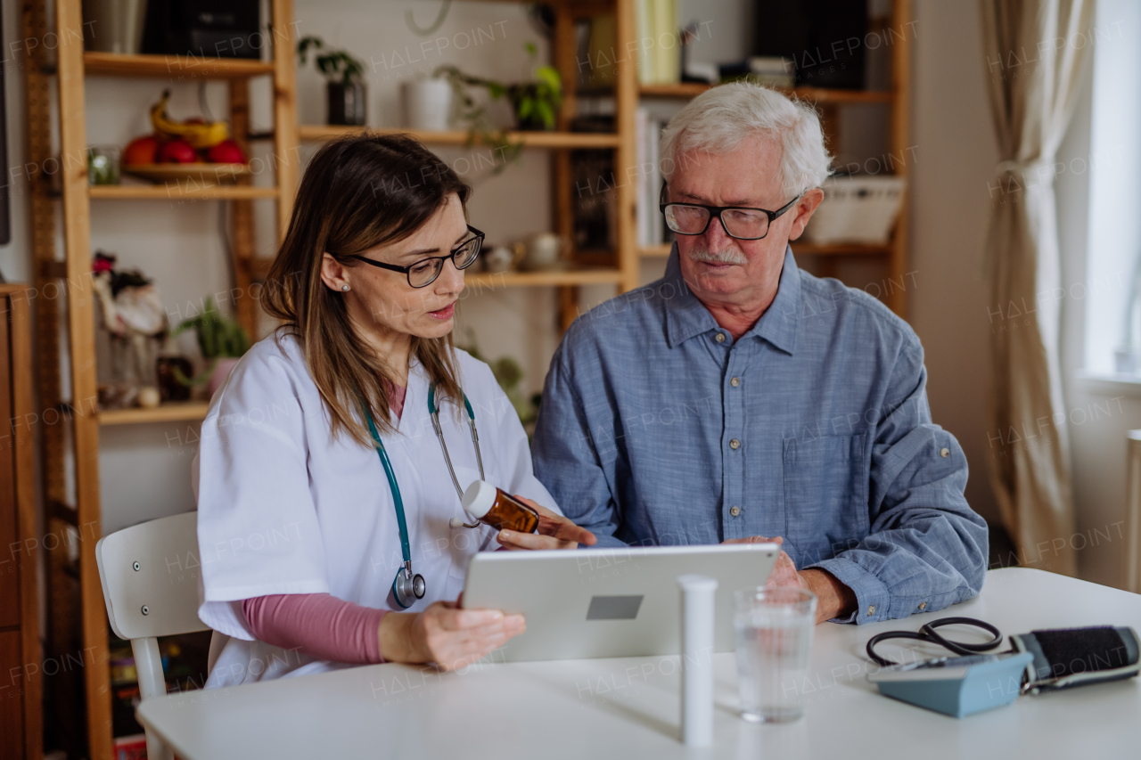 A healthcare worker or caregiver visiting senior man indoors at home, explaining medicine dosage.