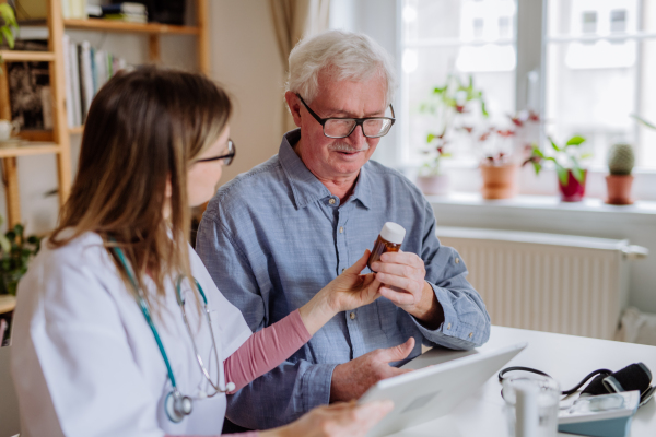 A healthcare worker or caregiver visiting senior man indoors at home, explaining medicine dosage.