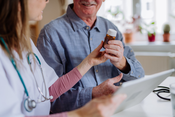 A healthcare worker or caregiver visiting senior man indoors at home, explaining medicine dosage.