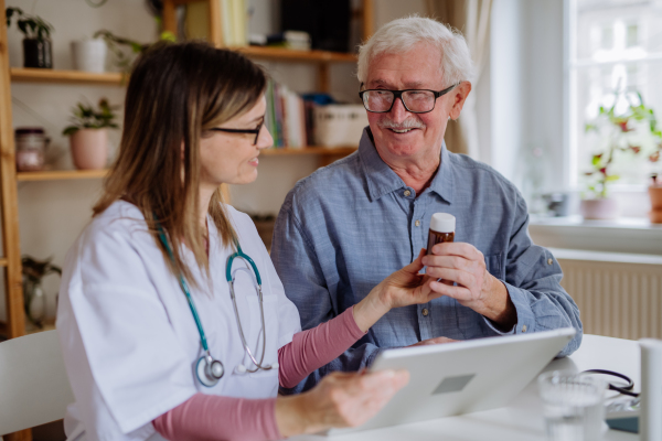 A healthcare worker or caregiver visiting senior man indoors at home, explaining medicine dosage.