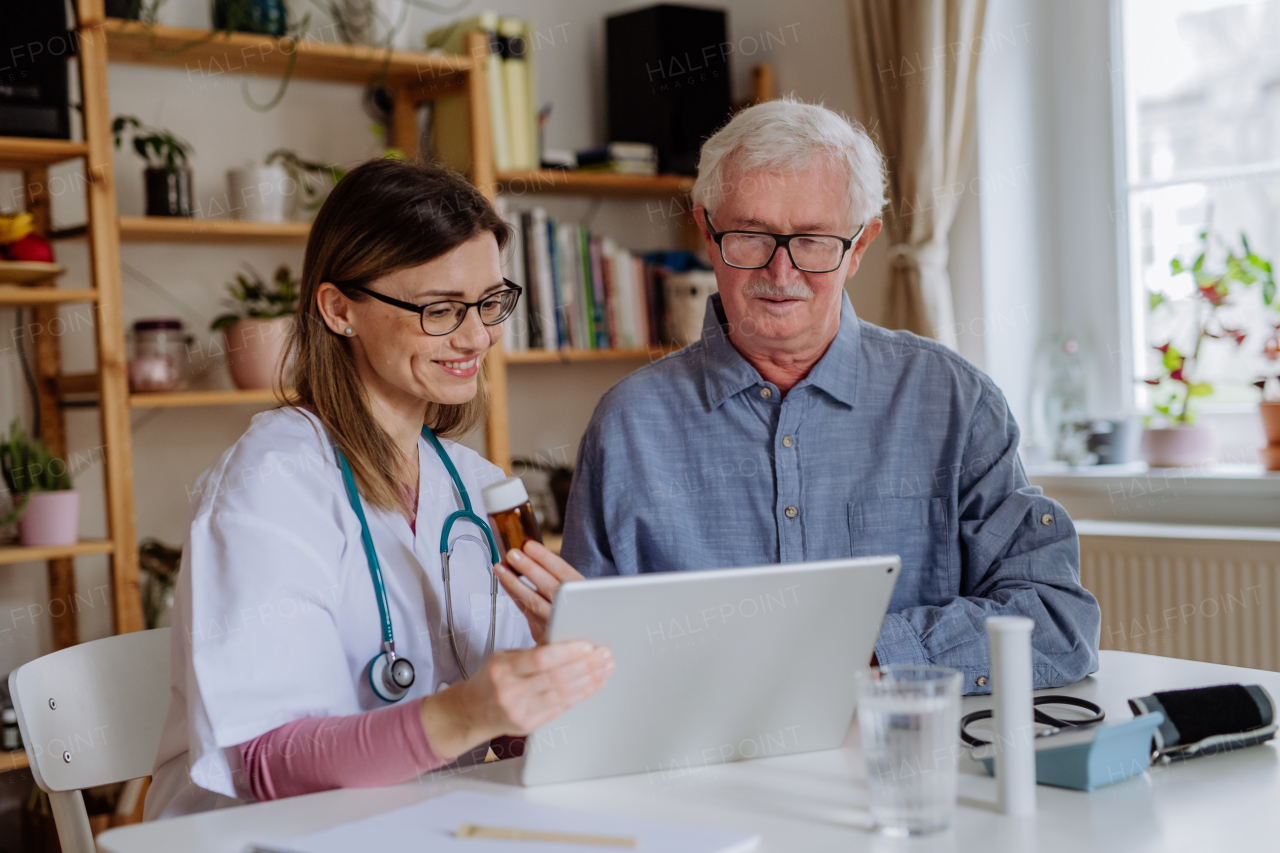 A healthcare worker or caregiver visiting senior man indoors at home, explaining medicine dosage.