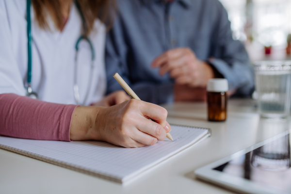 A healthcare worker or caregiver visiting senior man indoors at home, explaining medicine dosage.