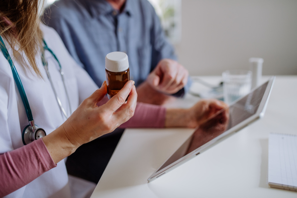 A healthcare worker or caregiver visiting senior man indoors at home, explaining medicine dosage.