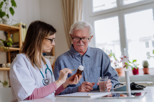 A healthcare worker or caregiver visiting senior man indoors at home, explaining medicine dosage.