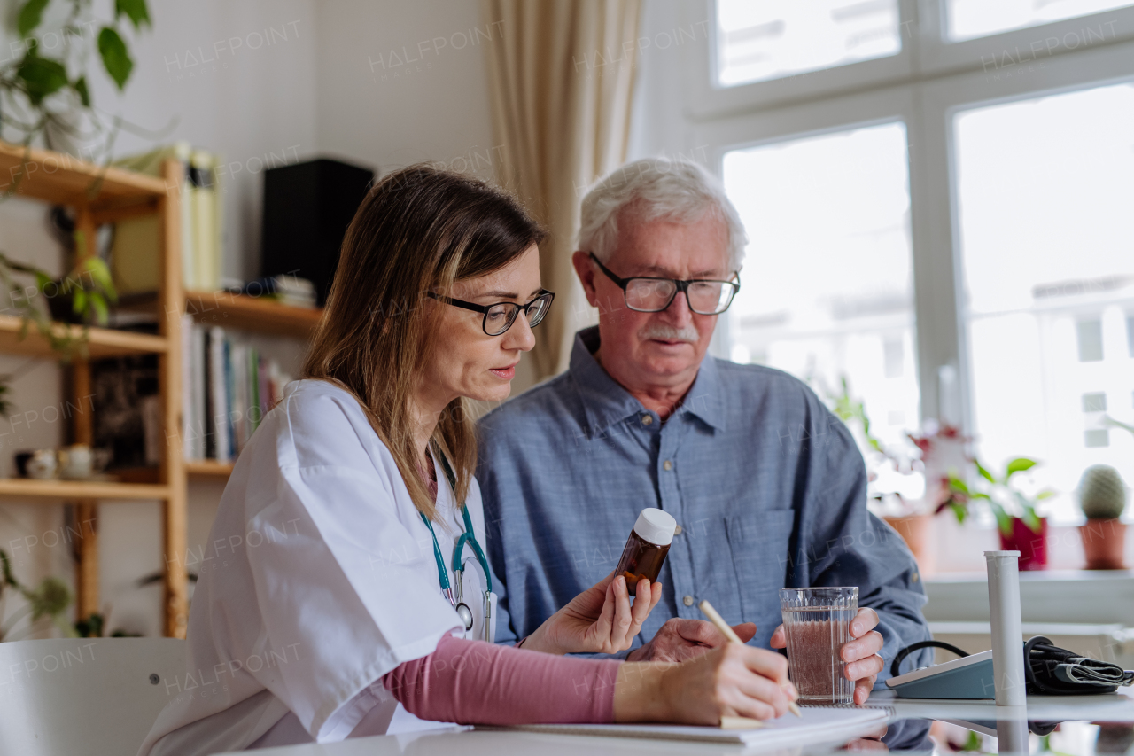 A healthcare worker or caregiver visiting senior man indoors at home, explaining medicine dosage.