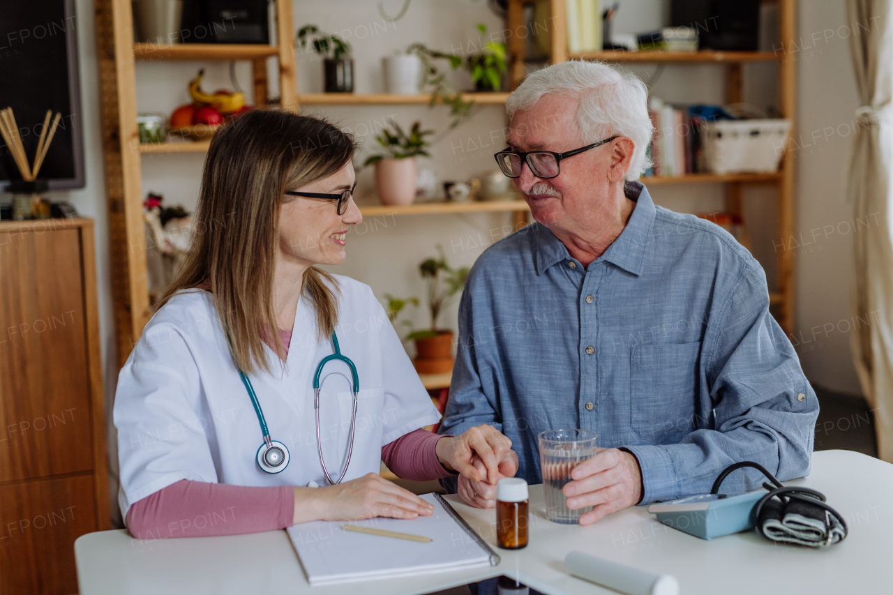 A healthcare worker or caregiver visiting senior man indoors at home, explaining medicine dosage.