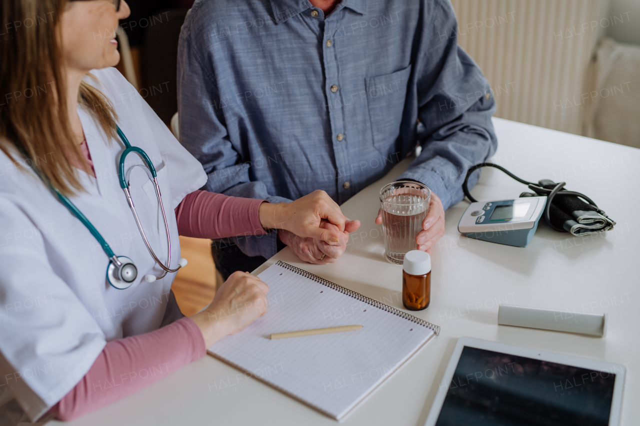 A close-up of doctor holding hand of senior patient and consoling him during medical visit at home.