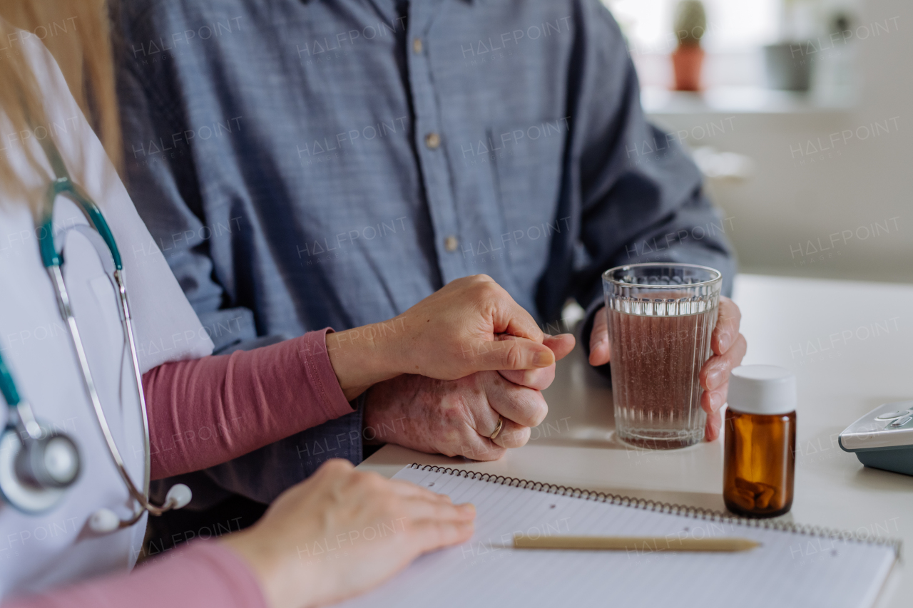 A close-up of doctor holding hand of senior patient and consoling him during medical visit at home.