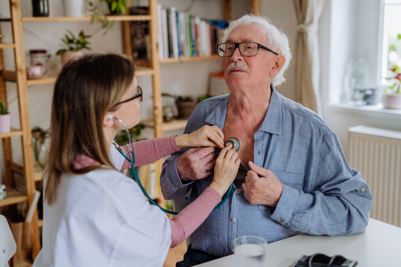 A female doctor visiting senior man and examinig him indoors at home.