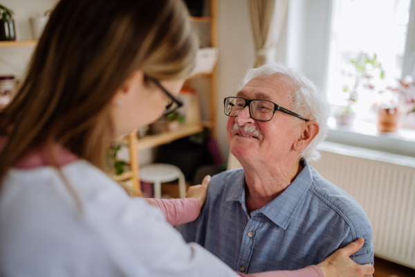 A healthcare worker or caregiver visiting senior man indoors at home.