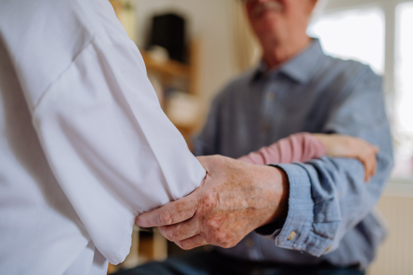 A close-up of doctor holding hand of senior patient and consoling him during medical visit at home.