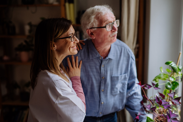 A healthcare worker or caregiver visiting senior man indoors at home, talking.