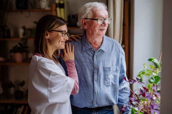 A healthcare worker or caregiver visiting senior man indoors at home, talking.