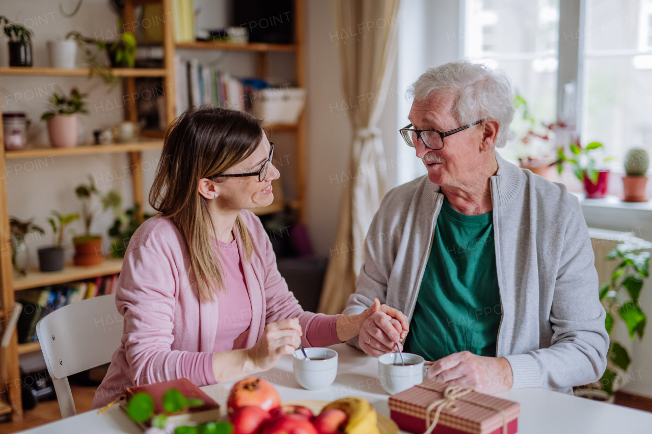 An adult daughter visiting her senior father at home and having coffee together, talking.