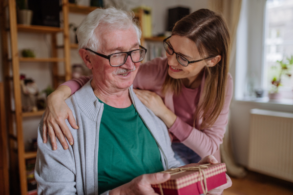 A happy woman surprising her senior father when visiting him at home and bringing present.