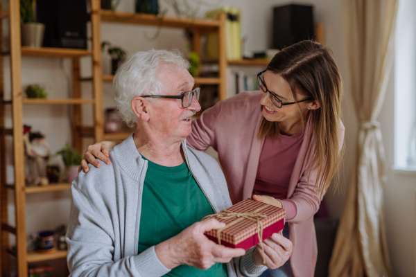 A happy woman surprising her senior father when visiting him at home and bringing present.