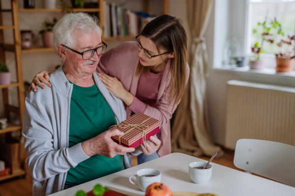 A happy woman surprising her senior father when visiting him at home and bringing present.