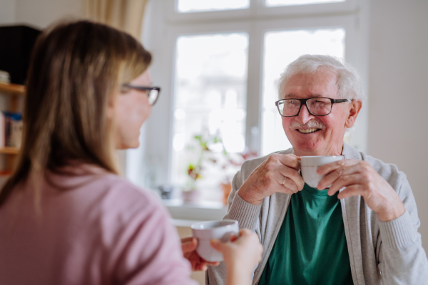 An adult daughter visiting her senior father at home and having coffee together, talking.