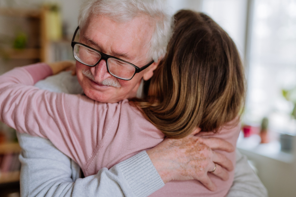 A rear view of adult daughter hugging her senior father when visitng him at home.